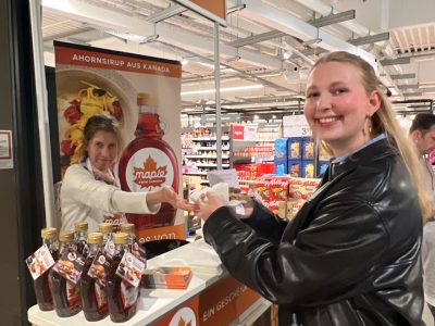 Eine Frau bekommt eine Waffel mit Ahornsirup vom Verkostungsstand überreicht.